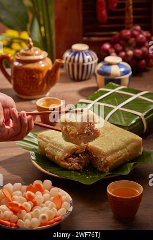 Main tenant un morceau de gâteau de riz collant (gâteau de Chung) sur le plateau Tet, fond pour la publicité de nourriture de vacances. Vue avant. Traditionnel nouvel an lunaire foo Banque D'Images