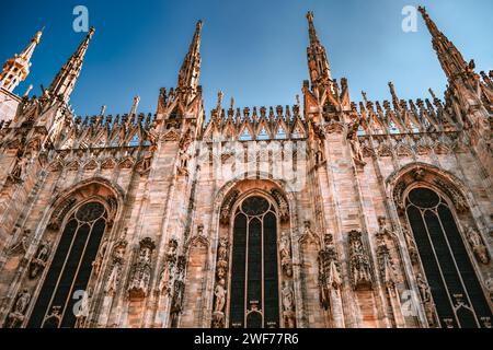 Les flèches montantes et les gravures de marbre complexes de la cathédrale emblématique de Milan se démarquent dans un ciel bleu clair, mettant en valeur la splendeur gothique. Banque D'Images