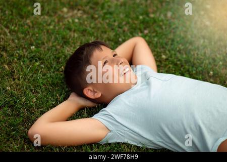 Souriant garçon heureux relaxant sur l'herbe verte. Ambiance week-end d'été. Modèles t-short pas d'impression, vous pouvez placer votre propre impression ou texte. Banque D'Images