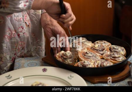 Gros plan des mains et des petits pains. Heureuse vieille femme Granny cuisine dans la cuisine petits pains à la cannelle et cuit des biscuits. Portrait, mise au point sélective, tonalité basse Banque D'Images