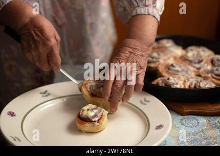 Gros plan des mains et des petits pains. Heureuse vieille femme Granny cuisine dans la cuisine petits pains à la cannelle et cuit des biscuits. Portrait, mise au point sélective, tonalité basse Banque D'Images