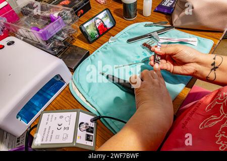 Une dame faisant ses ongles, en utilisant des coupe-ongles prêts à appliquer du vernis à ongles qui regardent une vidéo diffusée sur un téléphone portable Banque D'Images