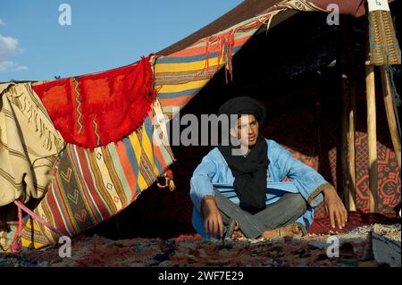 Un guide du désert en robe traditionnelle dans un camp de tentes avec des couvertures aux couleurs vives. Banque D'Images