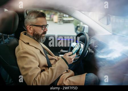 Gros plan d'un homme à l'aide de l'application de charge de véhicule électrique, vérifiant le niveau de la batterie sur le téléphone intelligent. Applications de charge pour surveiller la consommation d'électricité, localiser Banque D'Images