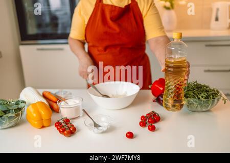 Une femme chef dans un uniforme verse l'huile d'olive d'une bouteille. Blogueuse alimentaire féminine caucasienne travaillant à expliquer comment cuisiner un plat Banque D'Images