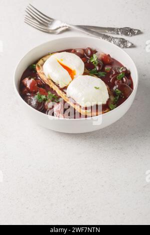 Oeufs pochés avec du pain grillé dans la sauce au vin rouge avec champignons, oignons et bacon gros plan dans une assiette sur la table. Vertical Banque D'Images