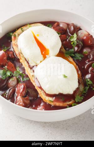 Oeuf poché de Bourgogne à la sauce au vin rouge sur toast oeuf en Meurette gros plan sur l'assiette sur la table. Vertical Banque D'Images