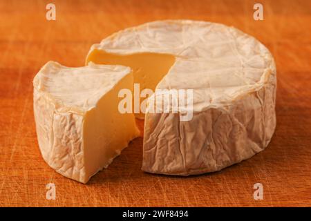 Camembert. Tête de fromage avec un morceau coupé sur une planche à découper en bois Banque D'Images