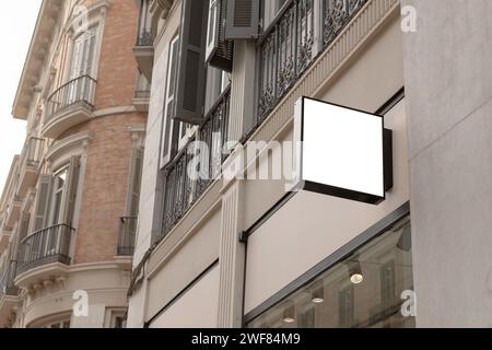 Enseigne de magasin vierge dans un cadre urbain classique, parfait pour les entreprises de superposer leur logo ou message dans un environnement réaliste. Enseigne carrée Banque D'Images