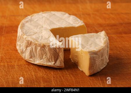 Camembert. Tête de fromage avec un morceau coupé sur une planche à découper en bois Banque D'Images