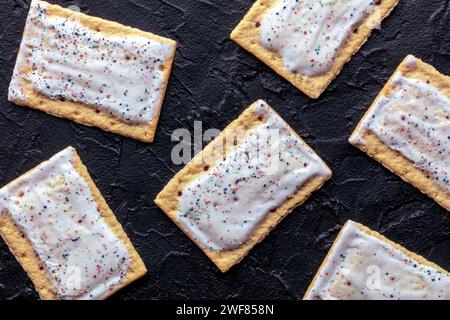 Disposition des tartes pop. Poptart grille-pain pâtisserie avec glaçage sur un fond d'ardoise noire, plan de pose plat au-dessus de la tête Banque D'Images