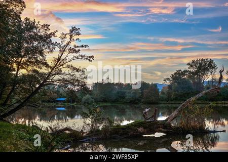 Lac au coucher du soleil. Beau ciel turquoise avec des nuages colorés Banque avec un tronc d'arbre tombé au premier plan. Surface d'eau calme. Bodovka, Slovaquie Banque D'Images