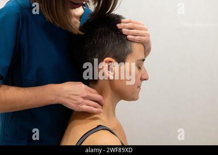 Un physiothérapeute en Blue Scrubs effectue un massage du cou sur une patiente aux cheveux courts Banque D'Images