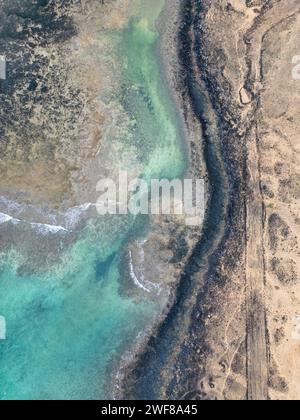 Vue aérienne des textures contrastées entre la mer turquoise et le terrain accidenté sur la côte nord de Fuerteventura près de Faro del Toston. Banque D'Images