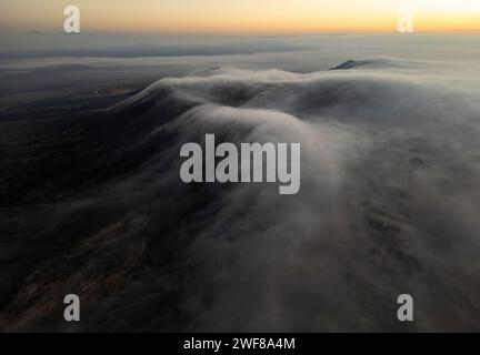 Des nuages mous tombent en cascade sur le paysage sombre de Fuerteventura alors que la première lumière du lever du soleil pointe sur l'horizon Banque D'Images