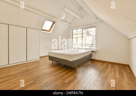 Cette chambre moderne et minimaliste dispose d''un grand lit, de plafonds inclinés, de parquet et d''une lucarne. Banque D'Images