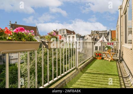 Un balcon urbain confortable orné de fleurs vibrantes et un petit coin salon, présentant un espace extérieur relaxant dans un cadre urbain. Banque D'Images