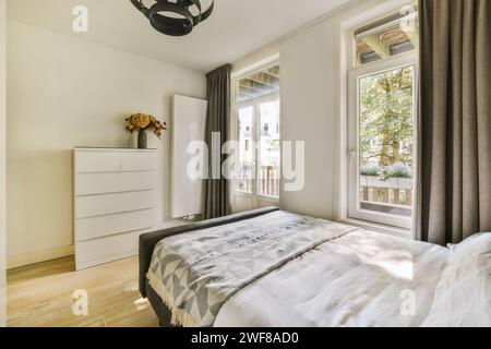 Chambre moderne confortable avec lit blanc, commode et accès à un balcon ensoleillé avec vue sur l'extérieur. Banque D'Images
