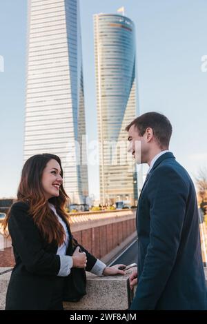 Deux professionnels s'engagent dans une conversation avec les gratte-ciel modernes de Madrid qui dominent en arrière-plan. Banque D'Images