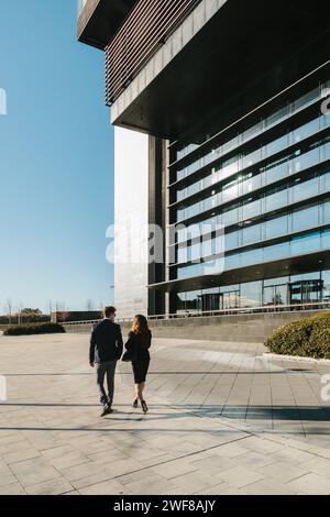 Un couple marche main dans la main, projetant des ombres par une journée ensoleillée à côté d'un bâtiment contemporain à Madrid. Banque D'Images