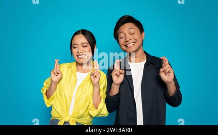 Homme et femme heureux en vêtements décontractés avec les yeux fermés, souriant et croisant les doigts pour bonne chance Banque D'Images