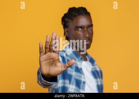 Jeune homme noir gestuelle ARRÊT avec paume ouverte sur fond de studio jaune Banque D'Images