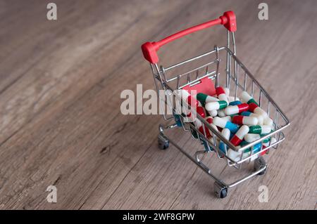 Un panier débordant de pilules colorées sur une table en bois. Copier l'espace pour le texte. Pharmacie en ligne, concept de coûts de santé. Banque D'Images