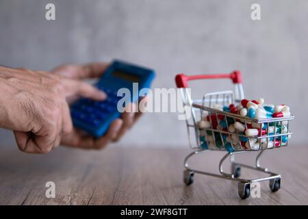 Un panier débordant de pilules colorées sur une table en bois et la main à l'aide d'une calculatrice. Coût croissant des médicaments d'ordonnance concept. Banque D'Images