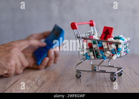 Un panier débordant de pilules colorées sur une table en bois et la main à l'aide d'une calculatrice. Coût croissant des médicaments d'ordonnance concept. Banque D'Images