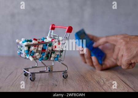 Un panier débordant de pilules colorées sur une table en bois et la main à l'aide d'une calculatrice. Coût croissant des médicaments d'ordonnance concept. Banque D'Images