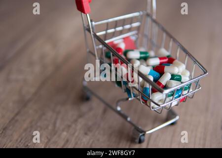 Un panier débordant de pilules colorées sur une table en bois. Copier l'espace pour le texte. Pharmacie en ligne, concept de coûts de santé. Banque D'Images