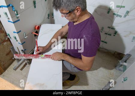 Tuile dans un petit espace mesurant et marquant une tuile pour l'installation d'un mur de tuile dans une rénovation de salle de bains. Concept de rénovation domiciliaire Banque D'Images