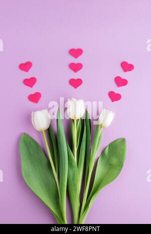 Ensemble de trois tulipes blanches avec des coeurs sur fond rose. Banque D'Images