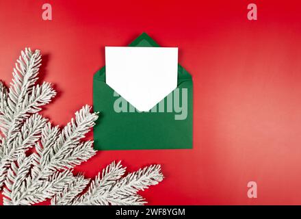 Vue de dessus de l'enveloppe verte, carte blanche et branches de sapin sur fond rouge. Noël, composition du nouvel an. Banque D'Images