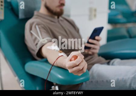 Homme caucasien méconnaissable serrant une balle de caoutchouc rouge au cours d'une transfusion sanguine dans un centre médical Banque D'Images