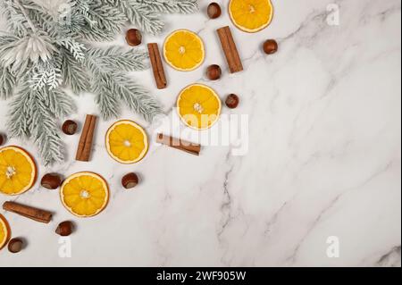 Composition de Noël, tranches d'orange séchées, branches de sapin, bâtonnets de cannelle, noisettes sur fond de marbre blanc. Noël, nouvel an, hiver conc Banque D'Images