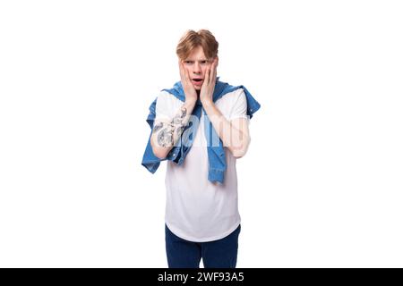 jeune homme aux cheveux rouges mince et émotionnel avec un tatouage sur ses bras est habillé d'une chemise bleue élégante Banque D'Images