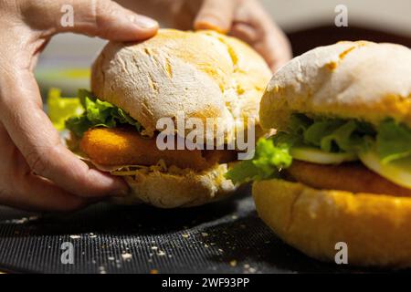 Sandwich au poisson avec laitue sur pain, tenu par les mains d'une femme. Banque D'Images