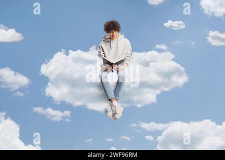 Jeune homme décontracté assis sur un nuage et lisant un livre dans le ciel Banque D'Images