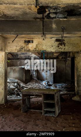 Une pièce abandonnée avec une grande table en bois et une chaise confortable placée à côté. Banque D'Images