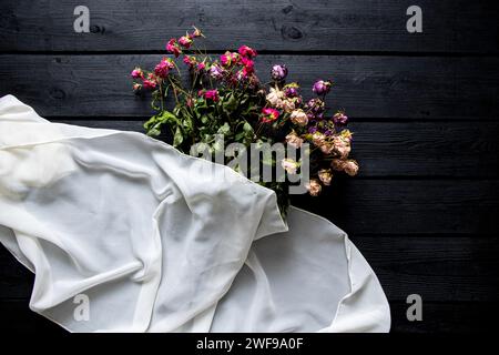 Un bouquet de roses séchées et un foulard blanc reposent sur une planche de bois noire, un bouquet de fleurs séchées sur la table Banque D'Images