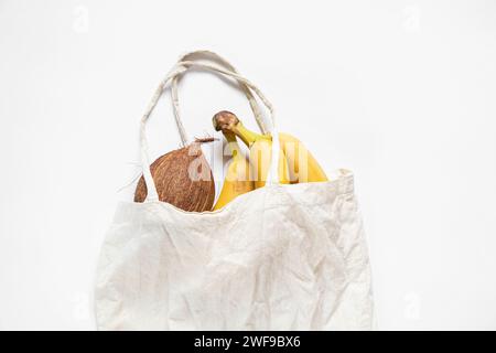 Noix de coco et bananes entières se trouvent dans un sac d'épicerie en tissu sur un fond blanc, fruits, nourriture Banque D'Images