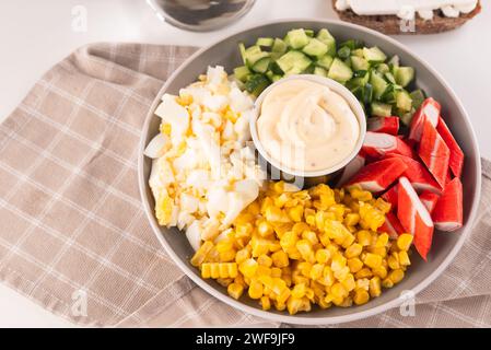 Salade de bâtonnets de crabe hachés avec maïs sucré, œufs, concombre et mayonnaise en pause dans le bol. Délices de fruits de mer. Banque D'Images