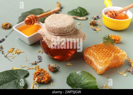 Pot avec miel savoureux, nid d'abeille, feuilles vertes et fleurs de pissenlit séchées sur fond vert, gros plan Banque D'Images