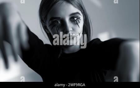 Petite fille avec maquillage Halloween effrayante regardant la caméra comme zombie. Portrait effrayant d'enfant en noir et blanc. Banque D'Images