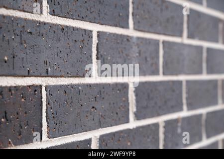 Mur de briques de maçonnerie incliné vers la droite. Pierres gris foncé et joints blancs. Profondeur de champ étroite Banque D'Images