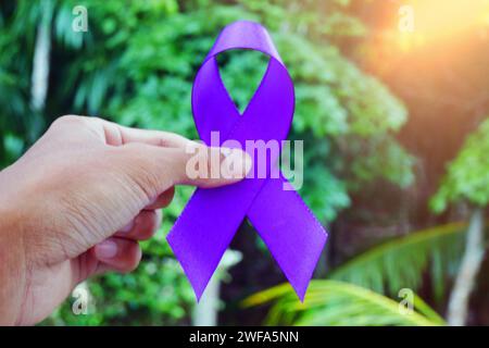 Homme tenant un ruban violet comme symbole de la Journée mondiale contre le cancer, gros plan. Banque D'Images