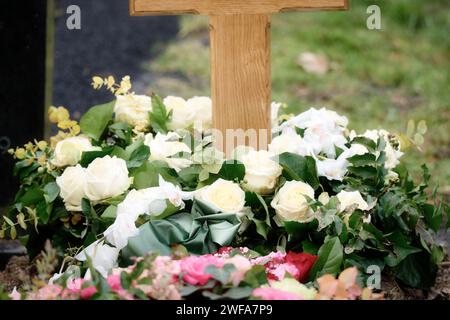 Couronne de fleurs funéraires de roses jaune clair et ruban gris-vert autour d'une croix en bois sur une tombe après un enterrement Banque D'Images