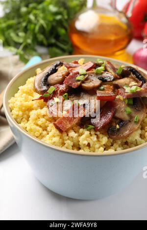 Savoureux porridge de millet avec des champignons, du bacon et de l'oignon vert dans un bol sur une table blanche, gros plan Banque D'Images