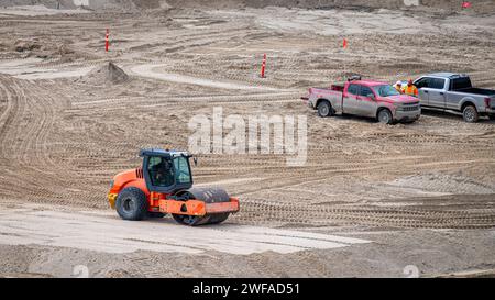 Compacteur vibrant à rouleaux de sol compactant une épaisseur de sable sur un chantier de construction, avec deux ramasseurs et des ouvriers Banque D'Images